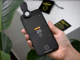 Hand holding a smartphone with the light meter diffuser clipped on and a reading displayed