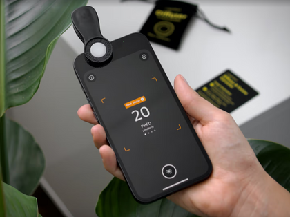 Hand holding a smartphone with the light meter diffuser clipped on and a reading displayed