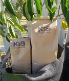 Two bags of mealworm frass insect fertilizer in front of leafy plants